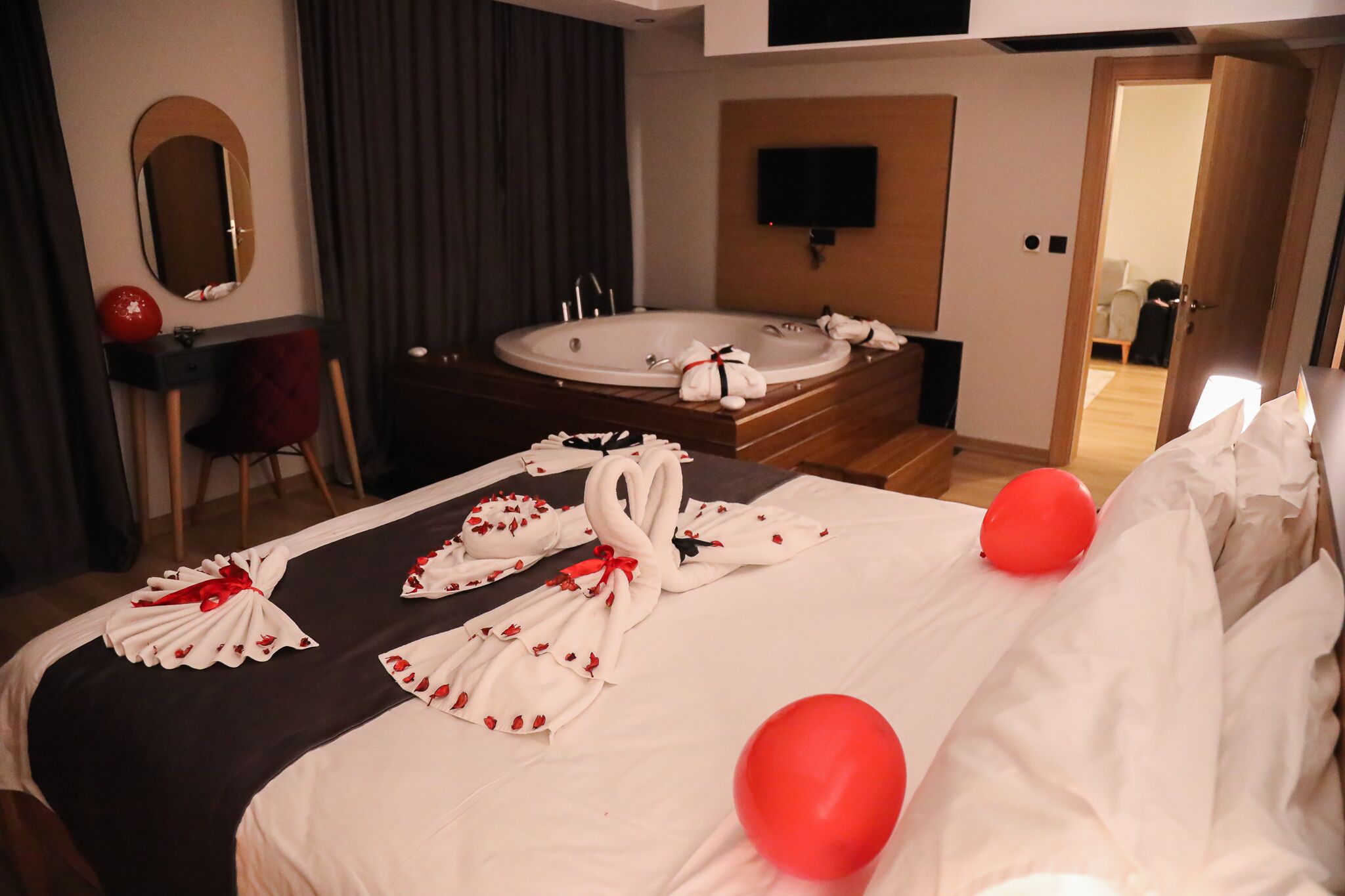 A hotel room with a large bed, a bathtub, a TV mounted on the wall, and a desk with a chair.