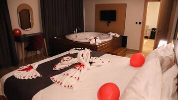 A hotel room with a large bed, a bathtub, a TV mounted on the wall, and a desk with a chair.