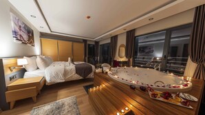 A modern hotel room with a large bed, a separate sitting area, a private balcony, and a jacuzzi. - Şehrar Suit Hotel (Surmene)