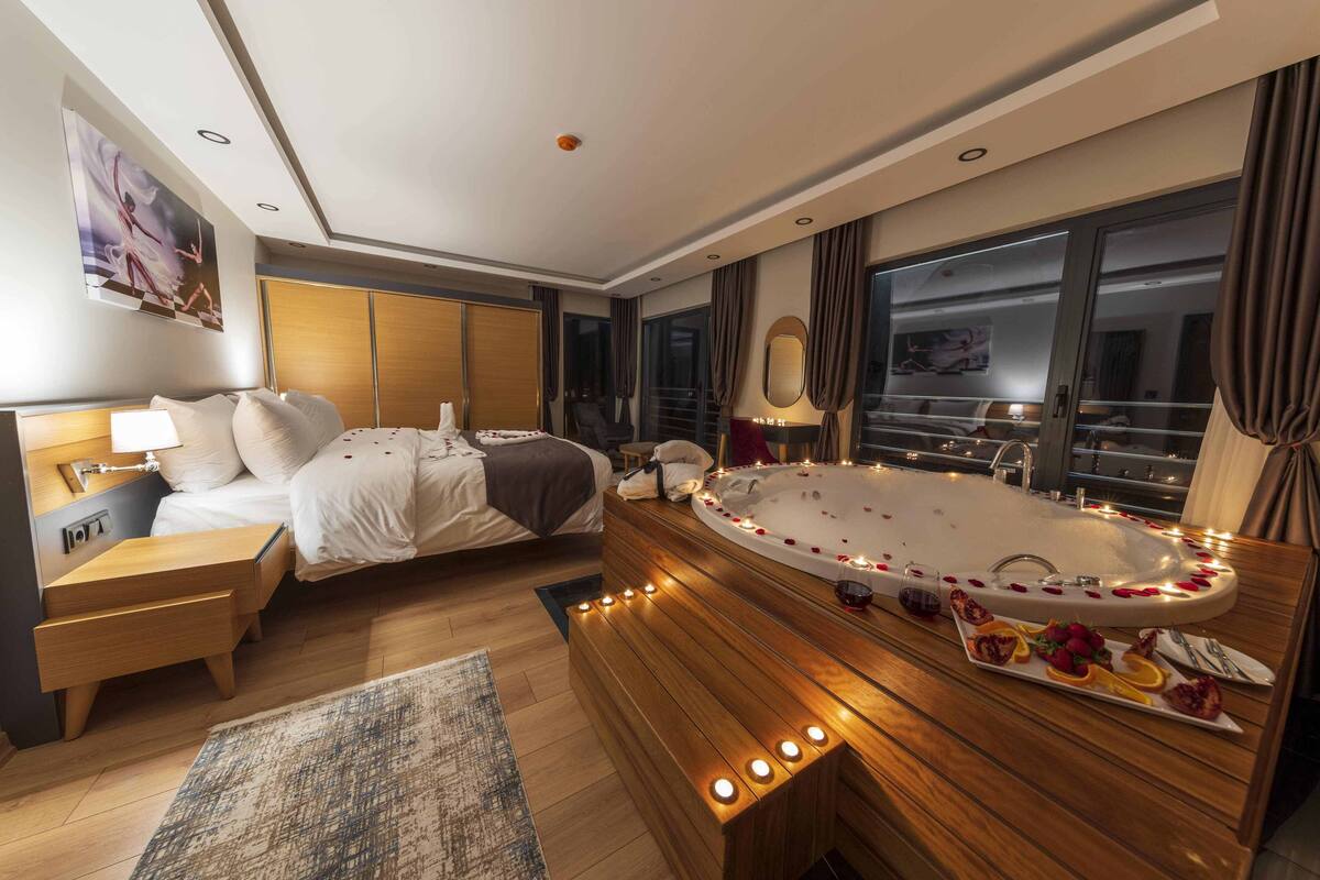 A modern hotel room with a large bed, a separate sitting area, a private balcony, and a jacuzzi.