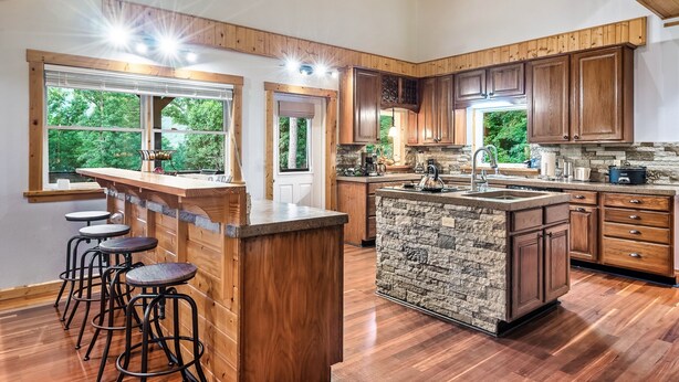 Cocina amplia con armarios de madera, una isla grande con taburetes y vistas al exterior.