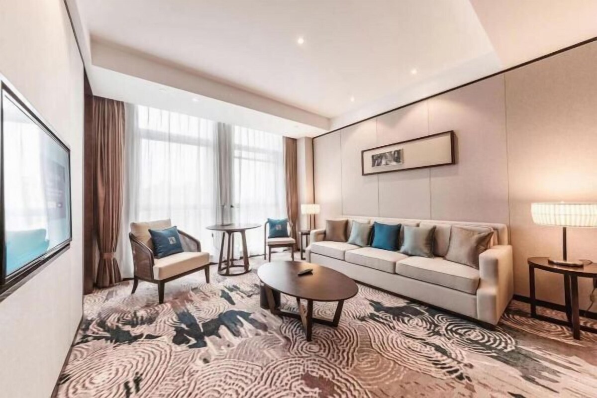 Een moderne hotelkamer met een groot raam, een bank, een stoel, een salontafel en een kamerkleed met dessin.