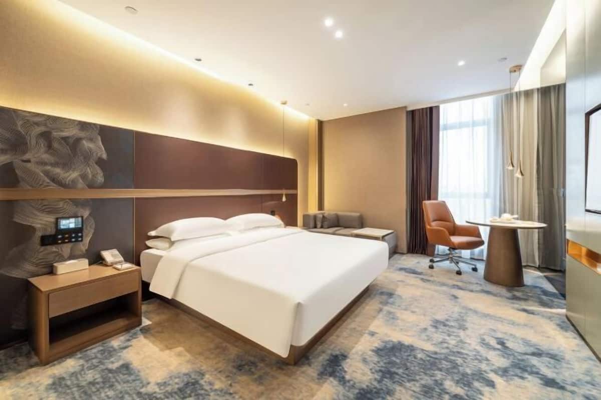 Une chambre d’hôtel moderne, dotée d’un grand lit, d’une table de chevet, d’une chaise et d’un bureau.