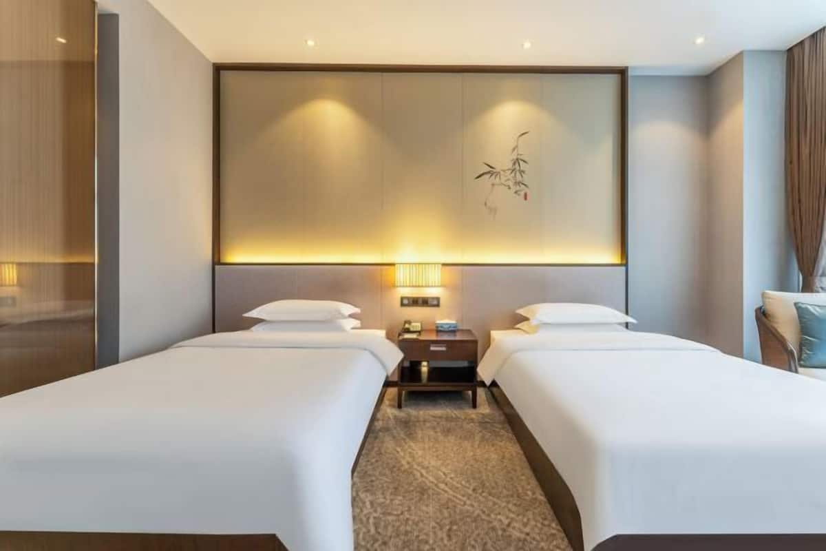 Une chambre d’hôtel avec deux lits, une grande œuvre d’art accrochée au mur, une table de chevet avec une lampe et une vue sur l’extérieur.