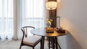 Une chambre d’hôtel avec une table ronde, une chaise, une lampe, un vase avec des fleurs et un panier de fruits.