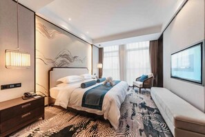 A modern hotel room with a large bed, a bedside table with a lamp, a seating area with a sofa, and a large window providing a view. - Fusheng Jiayue Hotel (Tai'an)
