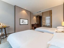 Una habitación de hotel con cama, escritorio, silla, espejo y un cuadro en la pared.