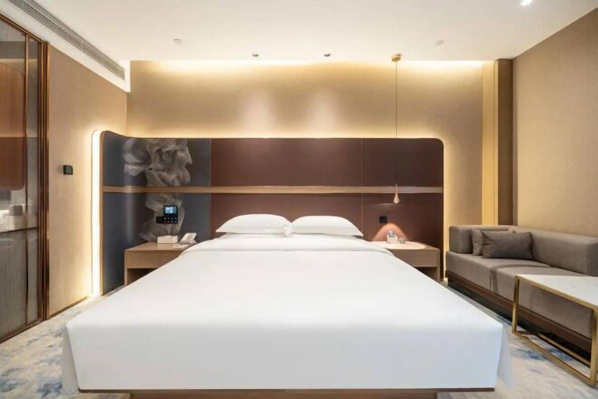 Une chambre d’hôtel moderne avec un grand lit, des tables de chevet, un canapé et une œuvre d’art accrochée au mur.