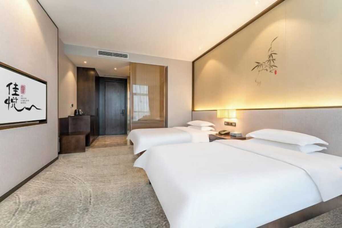 Une chambre d’hôtel avec un grand lit, des tables de chevet, une œuvre d  ’art accrochée au mur et donnant sur le couloir.