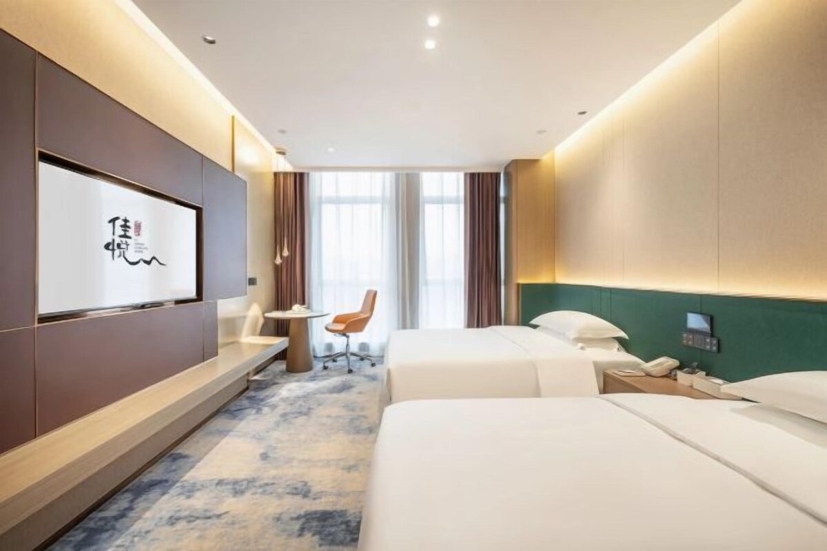 Ein Hotelzimmer mit zwei Betten, einem Schreibtisch, einem Sessel, einem Fernseher und einem Fenster mit Vorhängen.