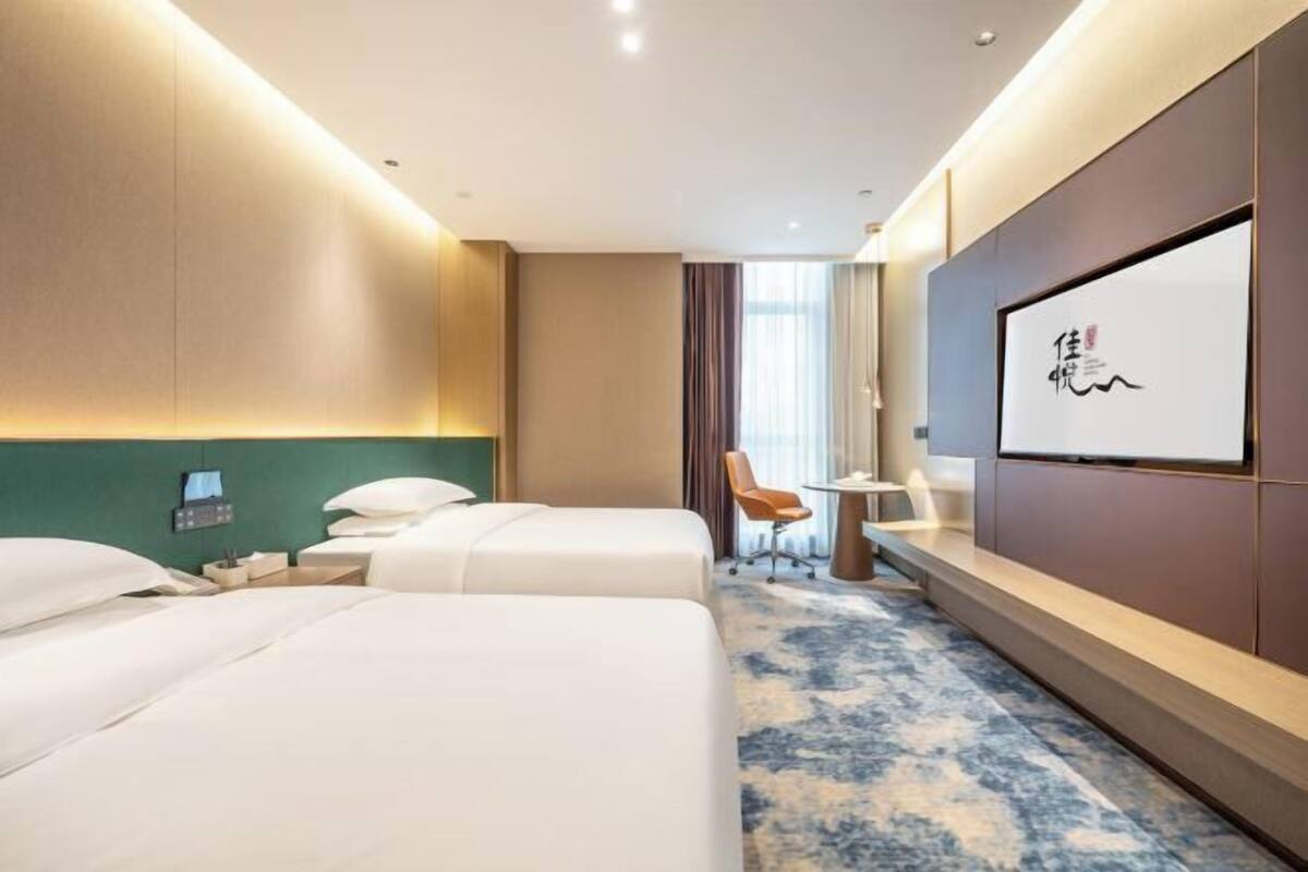 Une chambre d’hôtel avec deux lits, un bureau, une chaise, une télévision et une grande fenêtre.