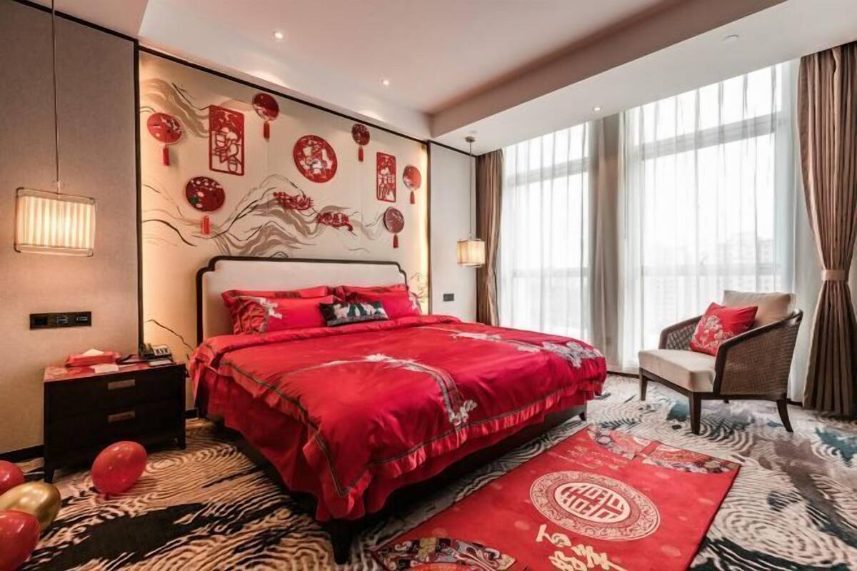 Une chambre d’hôtel avec un grand lit, une chaise, un mur agrémenté d’éléments décoratifs et une fenêtre avec des rideaux.