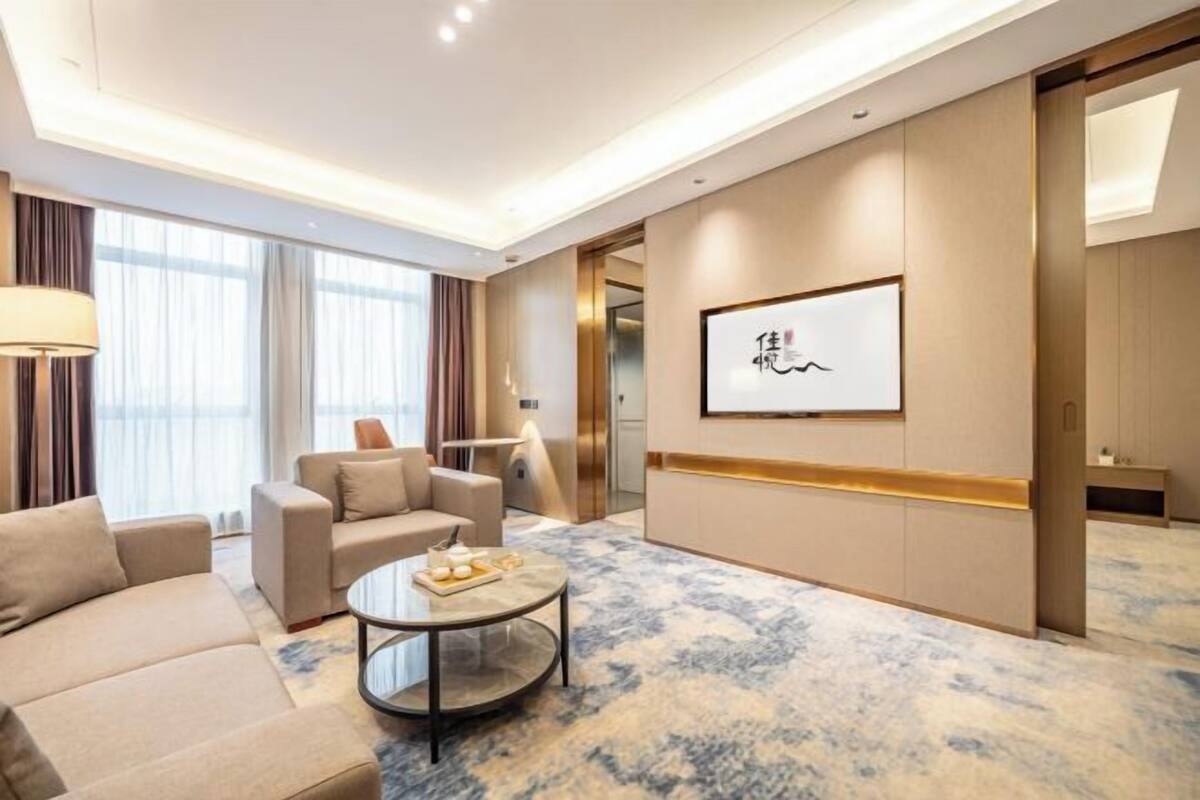 Une chambre d’hôtel moderne, équipée d’un canapé, d’un fauteuil, d’une table basse et ornée d’œuvres d’art au mur.