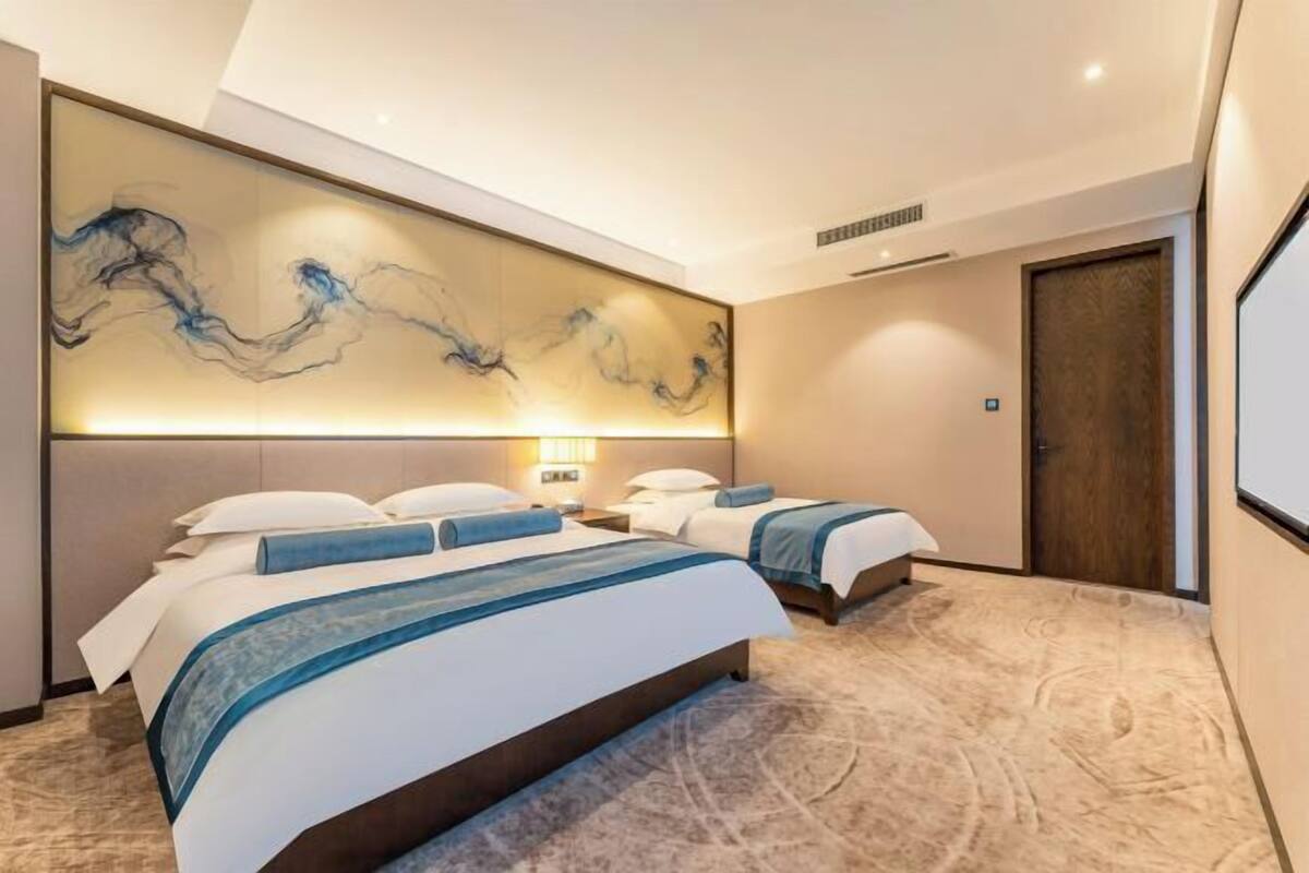 Une chambre d’hôtel avec deux lits, une grande œuvre d’art abstraite accrochée au mur, un sol recouvert de moquette et une porte.