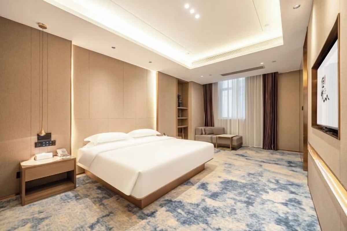 Een hotelkamer met een groot bed, nachtkastjes, een televisie en een raam met gordijnen.