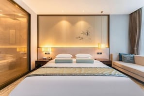 Een hotelkamer met een groot bed, nachtkastjes, een bank en een wand met een decoratief paneel.
