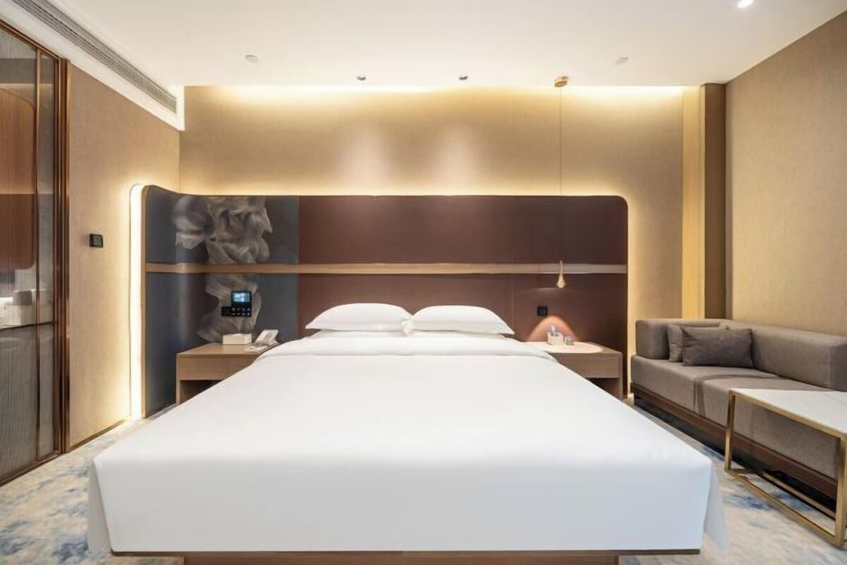 Een moderne hotelkamer met een groot bed, nachtkastjes, een bank en een kunstwerk aan de muur.