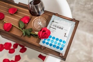 Un plateau avec des pétales de rose, un verre de vin rouge, une rose et un sac de bain jetable.