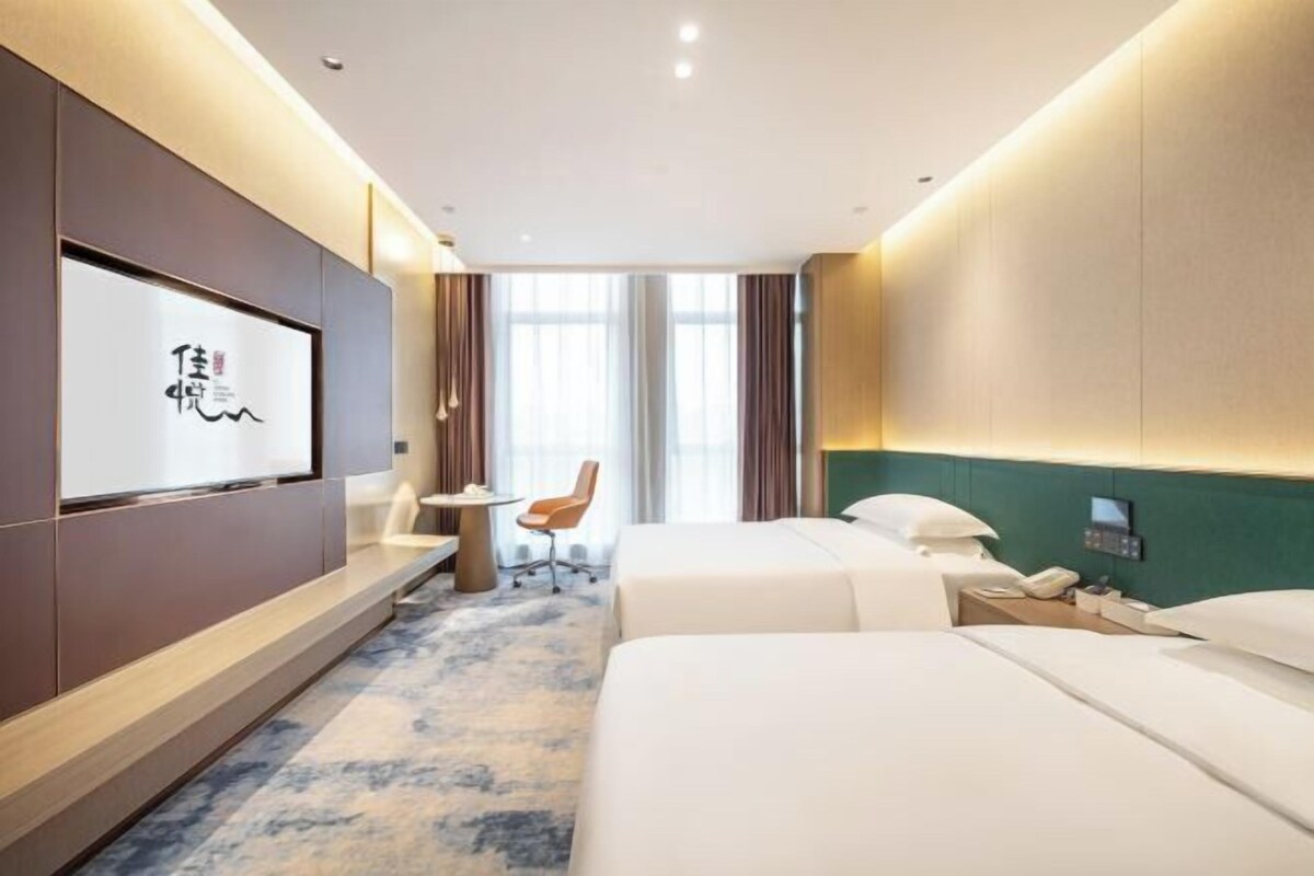 Ein Hotelzimmer mit zwei Betten, einem Schreibtisch, einem Sessel, einem Fernseher und Blick ins Freie.