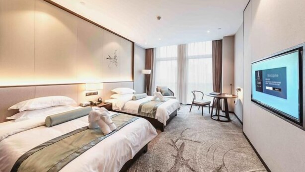 Une chambre d’hôtel avec deux lits, un bureau, une chaise, un écran de télévision et une grande fenêtre.