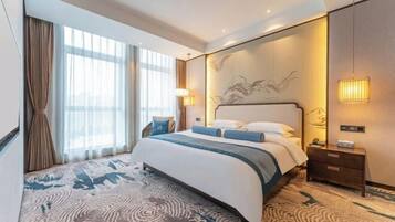 A hotel room with a large bed, a nightstand, a lamp, and a view of the city through the window.