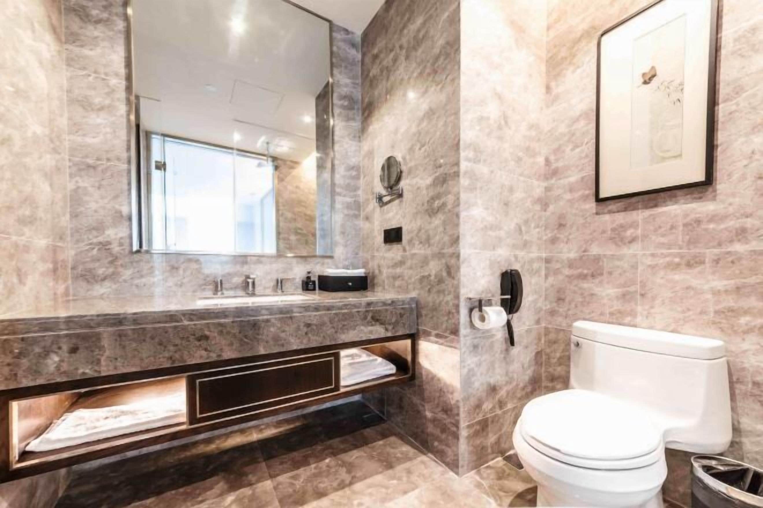 Un baño moderno con tocador de mármol, inodoro y un espejo grande.