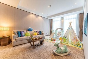 Een moderne hotelkamer met een bank, een salontafel, een speelruimte in tentstijl en een lamp.