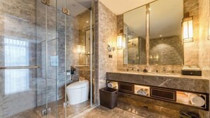 Une salle de bain moderne dotée d’une douche à parois de verre, d’un grand miroir et d’un meuble-lavabo en marbre avec un évier et un porte-serviettes.