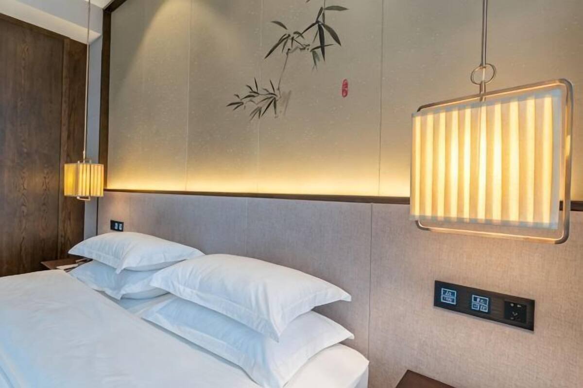 Une chambre d’hôtel avec un lit, un panneau de commande fixé au mur et une lampe suspendue.