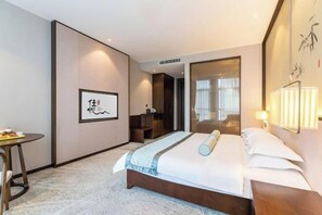 A hotel room with a bed, bedside table, lamp, and artwork on the wall. - Fusheng Jiayue Hotel (Tai'an)
