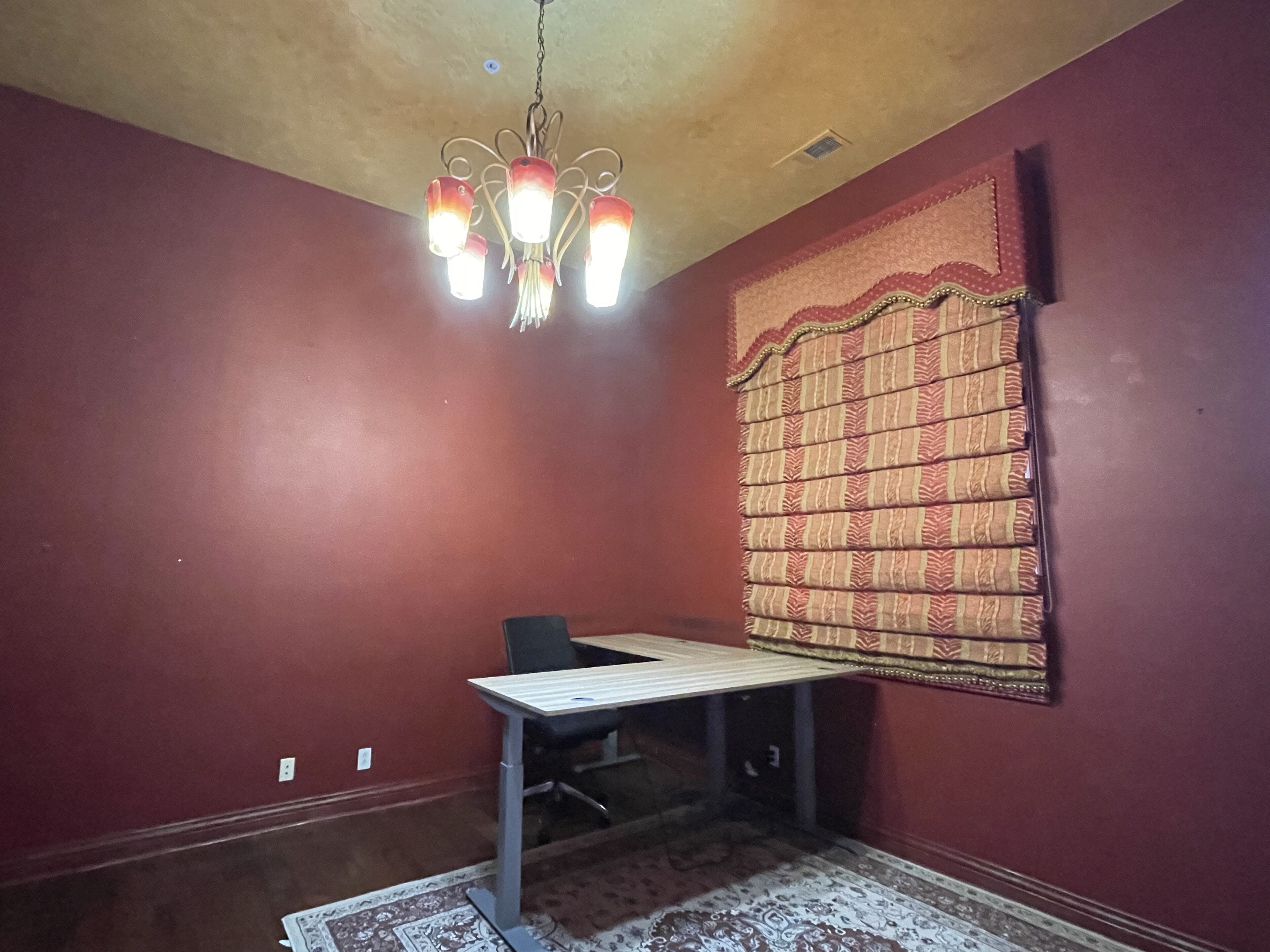A room with a table, a chair, a patterned curtain, and a chandelier.