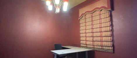 A room with a table, a chair, a patterned curtain, and a chandelier.