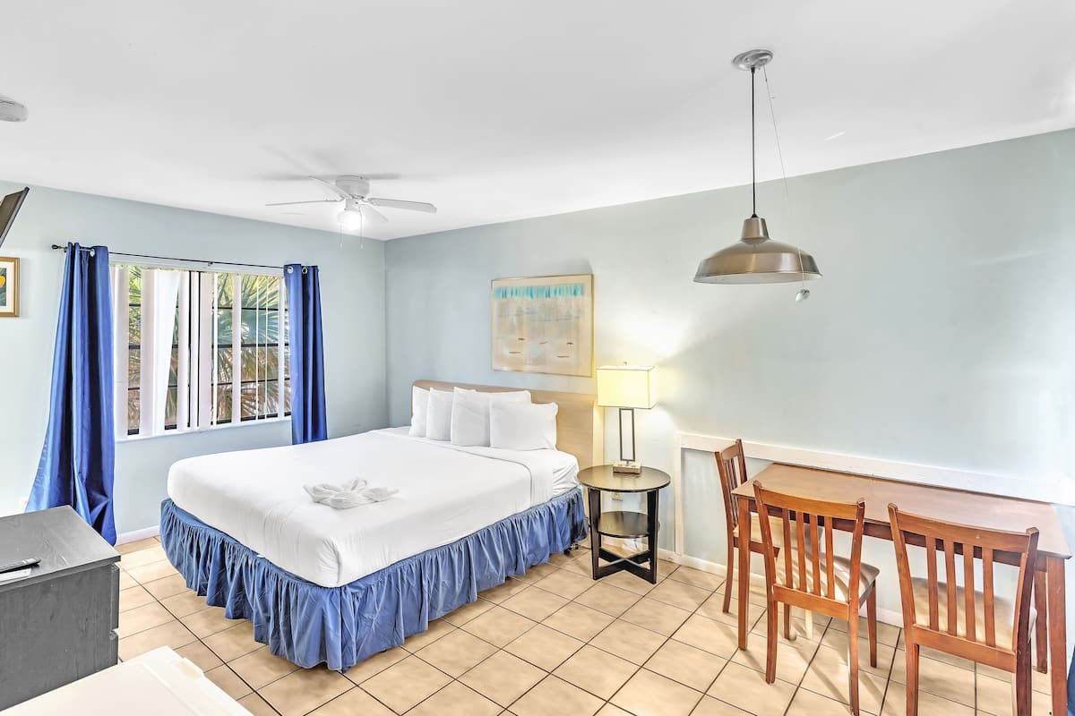 A hotel room with a bed, a desk, a chair, a lamp, and a ceiling fan.