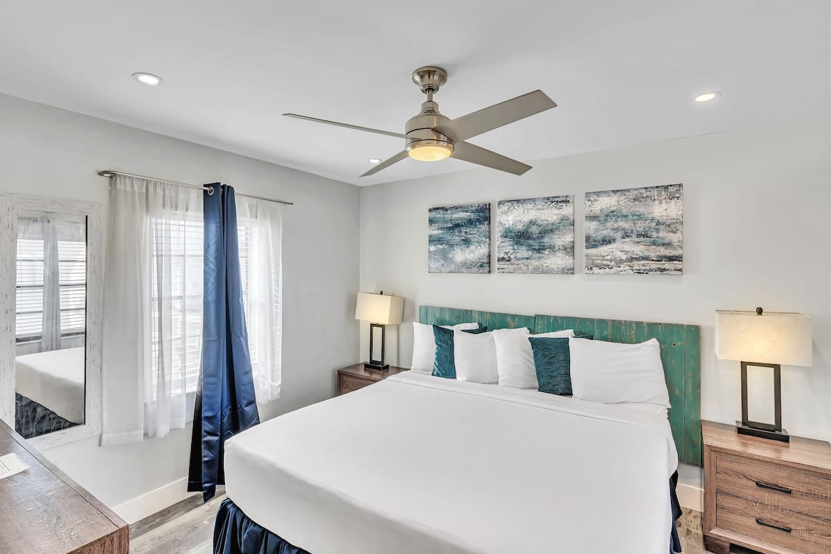 A hotel room with a bed, two bedside tables, a ceiling fan, and artwork on the wall.