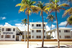 A white building with "neptune" signage, surrounded by palm trees, under a clear blue sky.