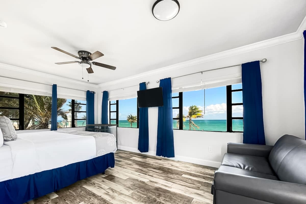 A bedroom with a bed, a ceiling fan, a TV, and a view of the ocean.