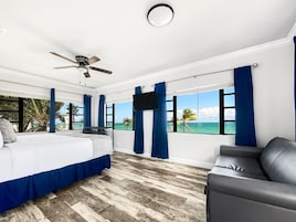 A bedroom with a bed, a ceiling fan, a TV, and a view of the ocean.
