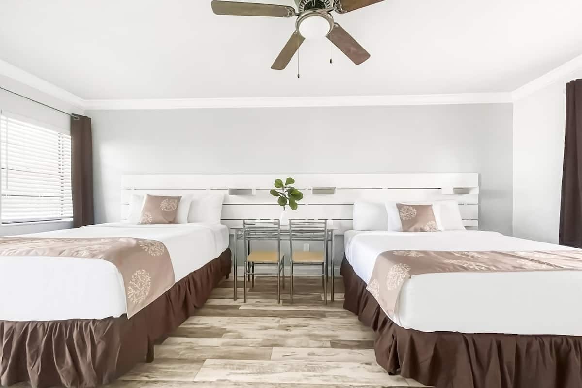 A hotel room with two beds, a desk, and a ceiling fan.