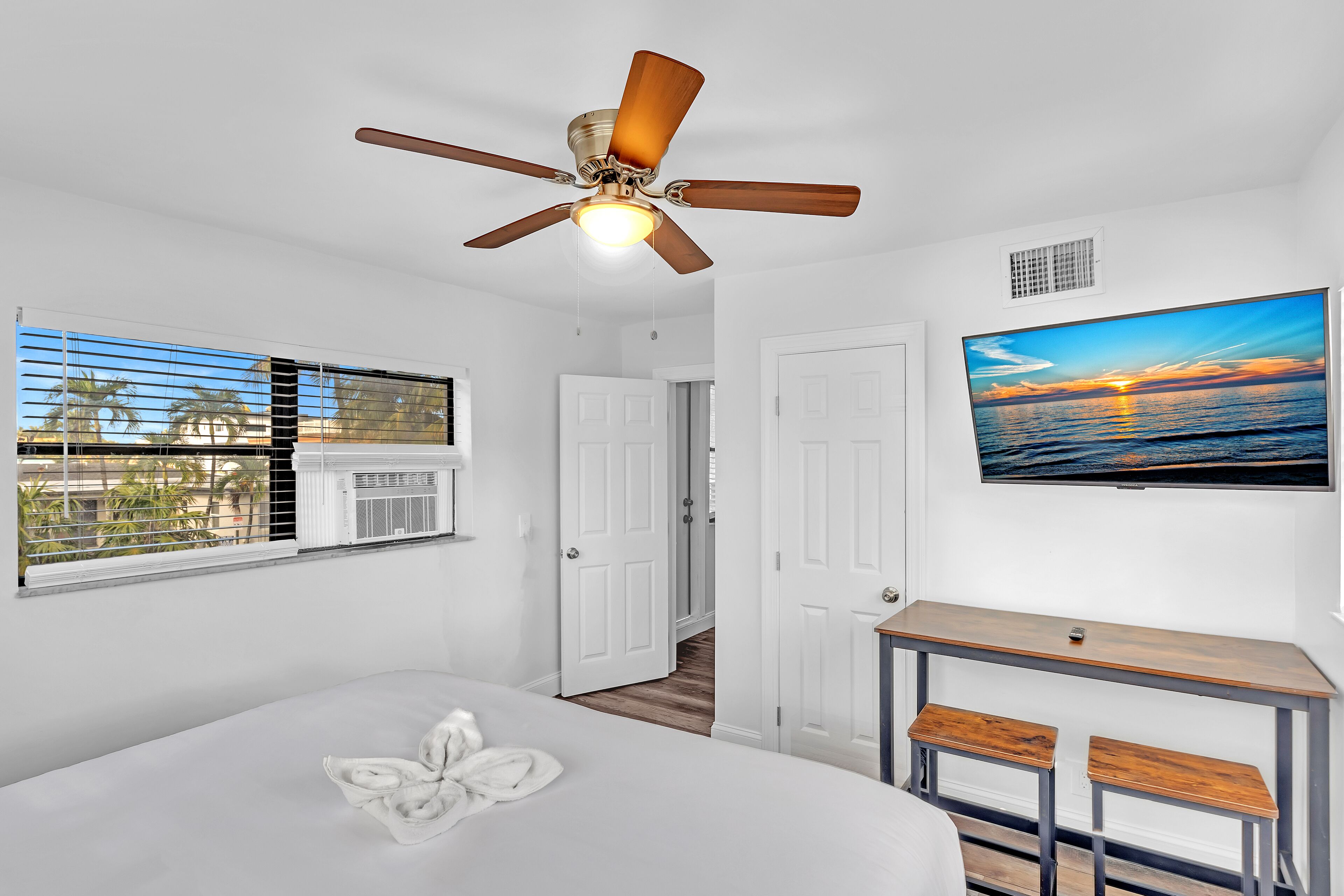 A bedroom with a bed, a ceiling fan, a TV, and a window with blinds.