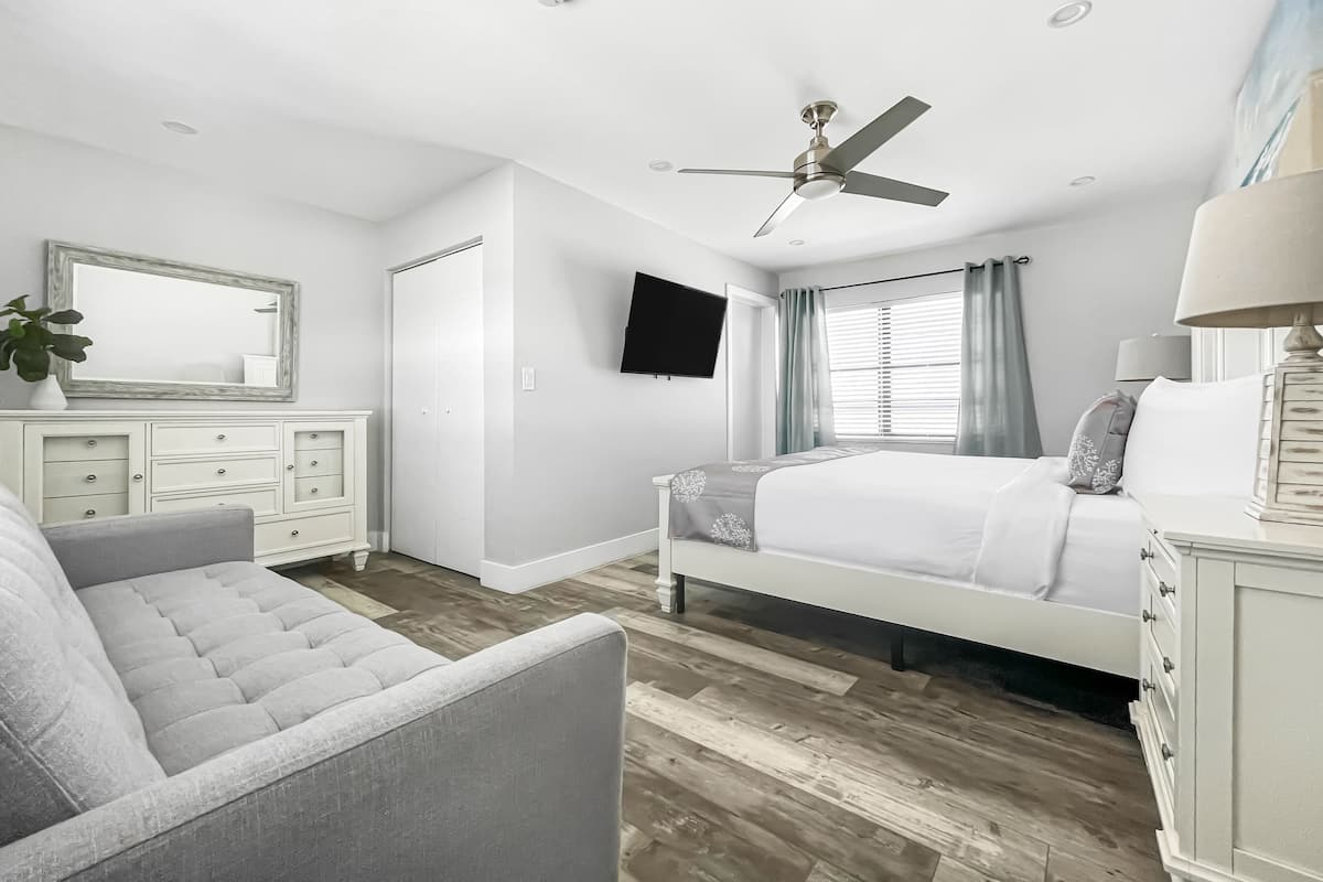 A bedroom with a bed, a chair, a dresser, a TV, and a ceiling fan.