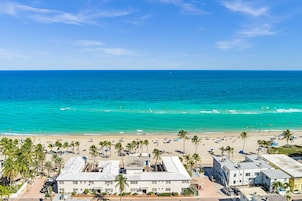 A beachside hotel with a view of the ocean, palm trees, and beachgoers.