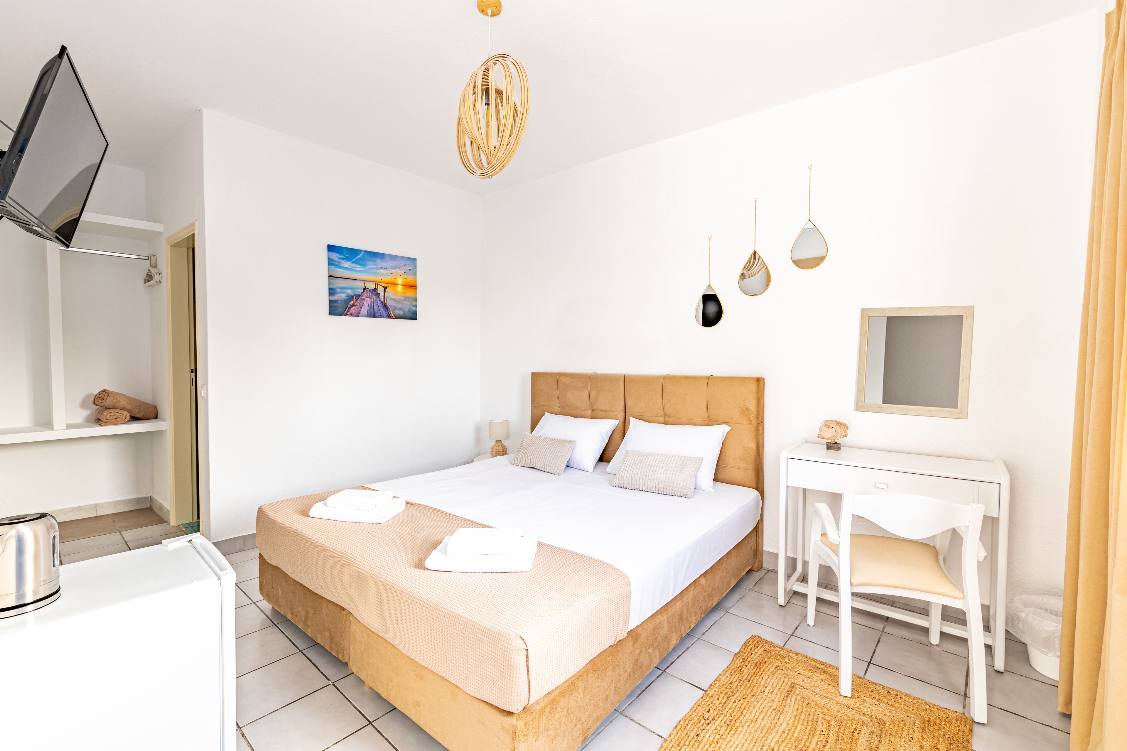 A modern hotel room with a bed, desk, and chair, a small desk lamp, and a painting on the wall.
