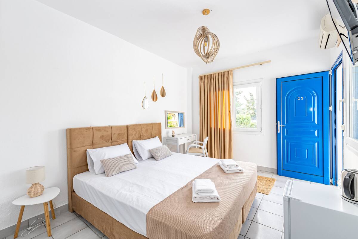 Een moderne hotelkamer met een groot bed, een bureau, een stoel, een blauwe deur en een kleine tafel met een lamp.