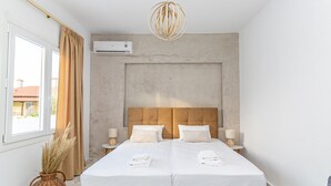 Habitació d'hotel amb dos llits, una finestra gran amb cortines, aire condicionat fixat a la paret, llum penjant de fibra natural i una taula petita amb làmpada.