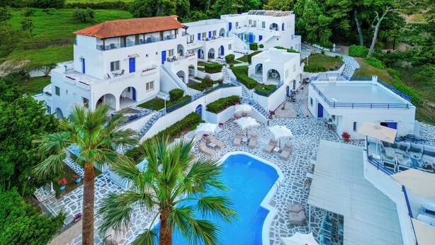 Un complex turístic amb una piscina, palmeres i un edifici blanc amb accents blaus.
