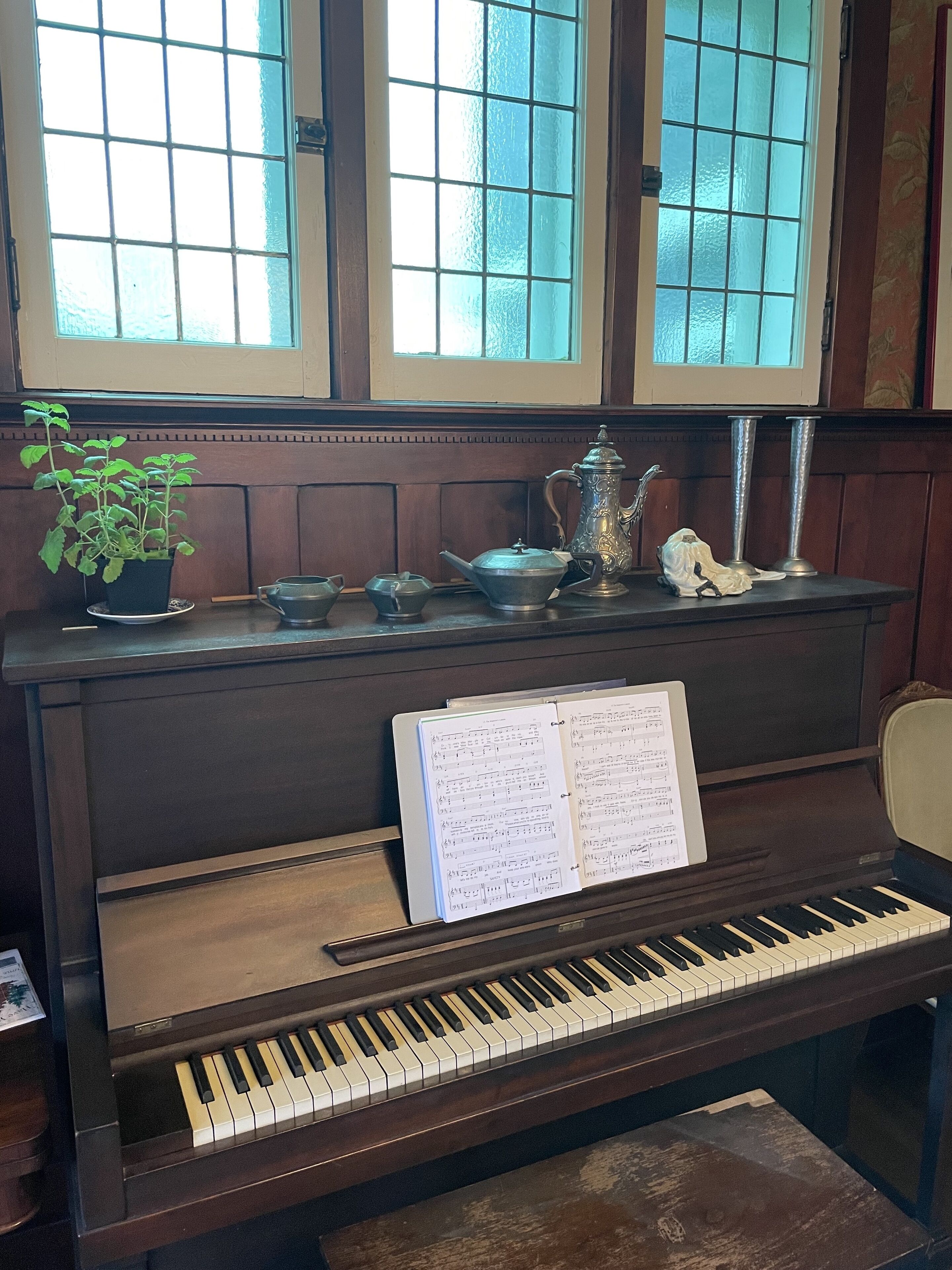 Un piano avec des partitions, une plante en pot et un pichet décoratif en métal, le tout posé sur une table en bois.