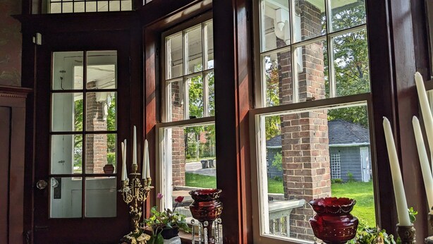 Ein Zimmer mit großen Fenstern, einer Tür und einer Fensterbank mit Kerzen und einer Vase.