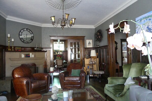 A spacious living room with leather armchairs, a chandelier, a clock, and a vase of orchids. - The Captain's House bed & breakfast (Midland)