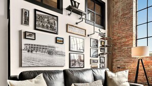 Un salon moderne avec un canapé en cuir noir, un tapis à motifs et un mur en briques.