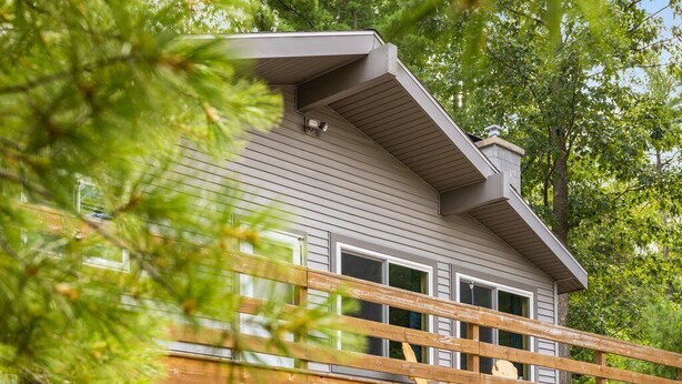 Ein zweistöckiges Haus mit überdachter Terrasse, einer Holzterrasse und einem kleinen Schuppen.